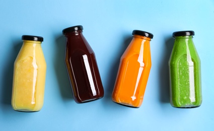 Photo of Bottles with delicious colorful juices on light blue background, flat lay