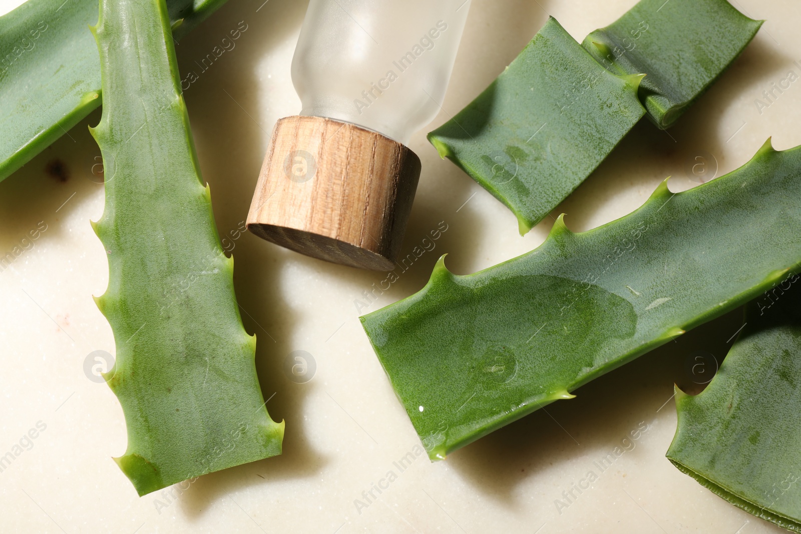Photo of Slices of fresh aloe vera leaves with gel and bottle on light table, flat lay
