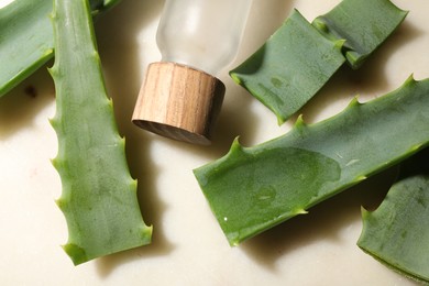 Slices of fresh aloe vera leaves with gel and bottle on light table, flat lay