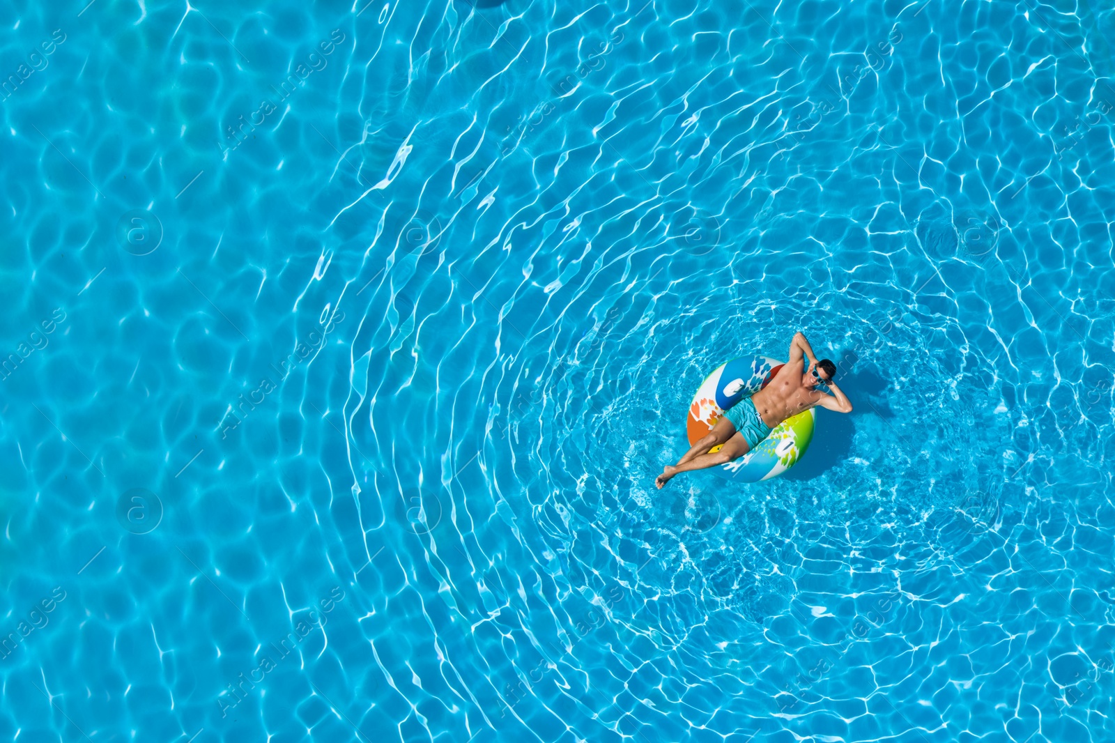 Image of Young man with inflatable ring in swimming pool, top view. Space for text