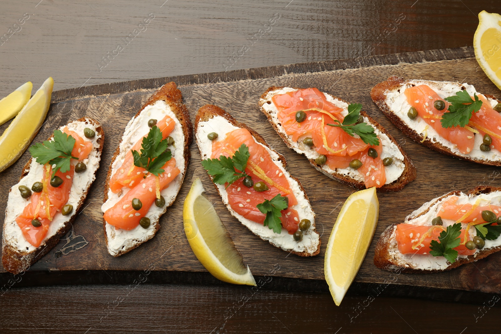 Photo of Tasty canapes with salmon, capers, lemon and cream cheese on wooden table, top view