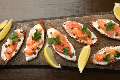 Photo of Tasty canapes with salmon, capers, lemon and cream cheese on wooden table, top view