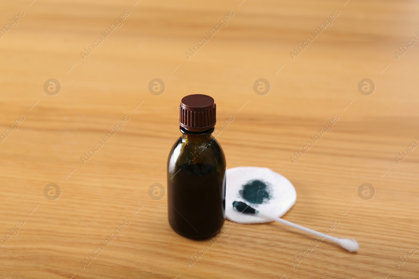 Photo of Bottle of brilliant green, cotton bud and pad on wooden table