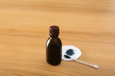 Bottle of brilliant green, cotton bud and pad on wooden table