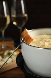 Fondue with tasty melted cheese, fork and piece of bread on table, closeup