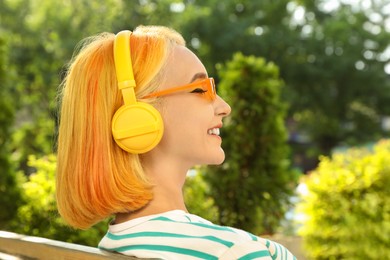 Photo of Beautiful young woman with bright dyed hair listening music in park