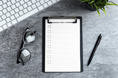 Photo of Clipboard with checkboxes, computer keyboard, eyeglasses and pen on grey table, flat lay. Checklist