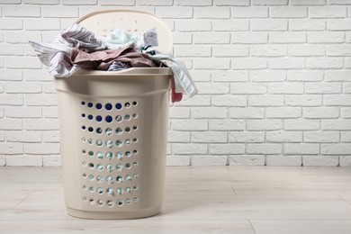 Laundry basket with clothes near white brick wall. Space for text