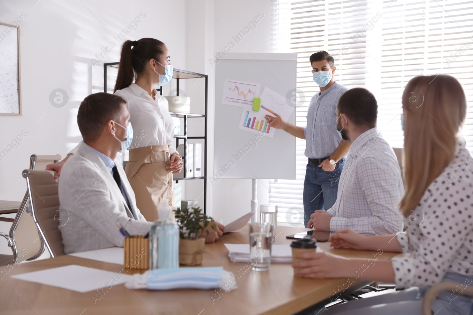 Photo of Group of coworkers with protective masks in office. Business meeting during COVID-19 pandemic