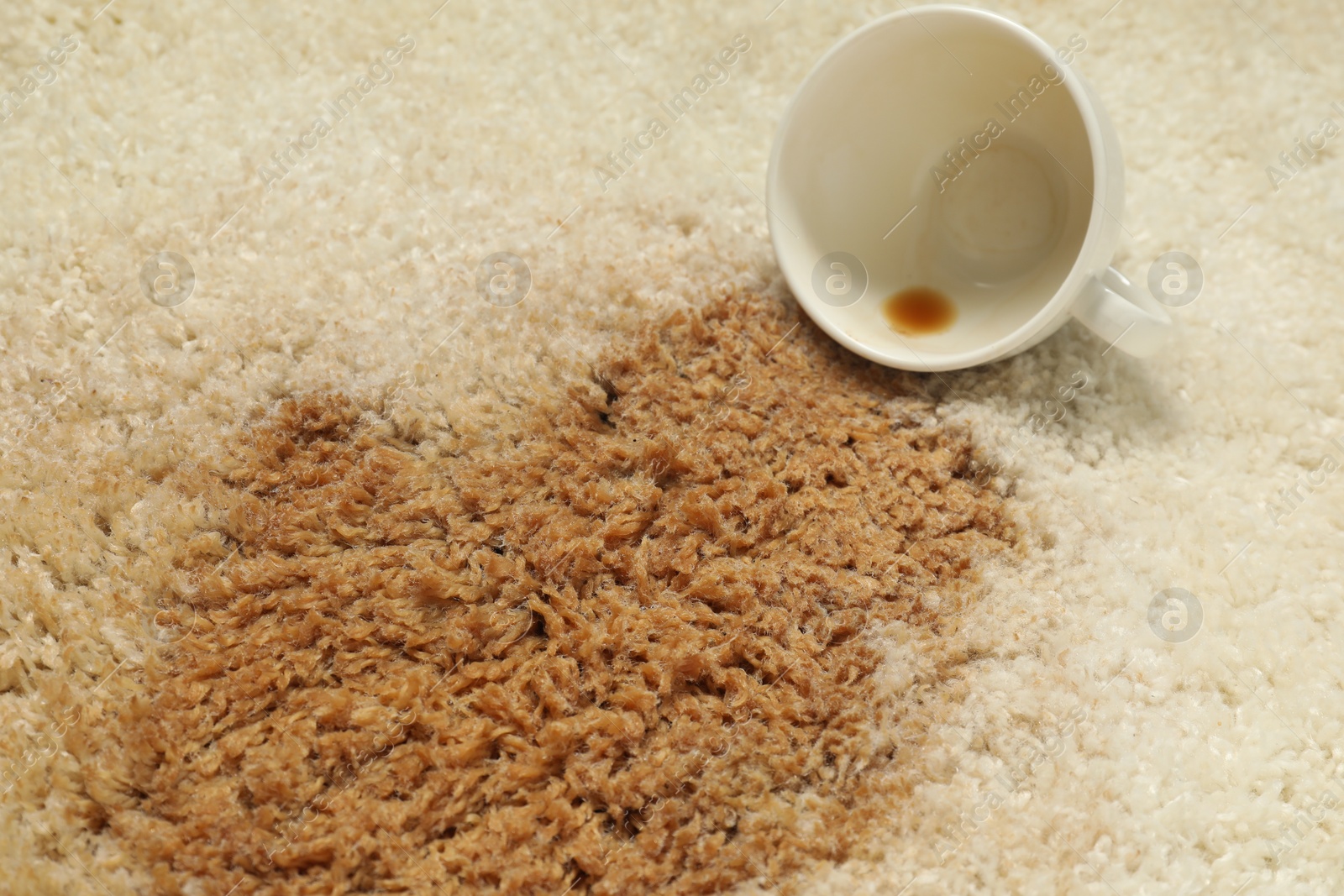 Photo of Overturned cup and spilled coffee on beige carpet, closeup