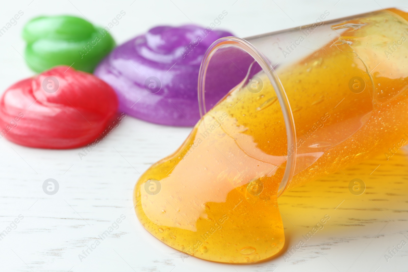 Photo of Different bright slimes on white wooden background, closeup