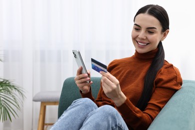 Photo of Happy young woman with smartphone and credit card shopping online on sofa at home