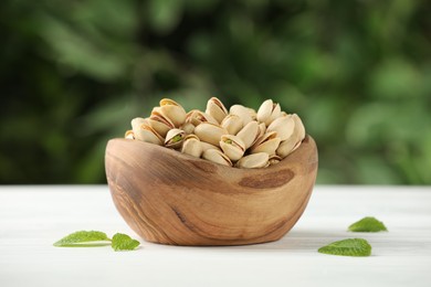 Tasty pistachios in bowl on white table against blurred background