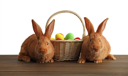 Cute bunnies and basket with Easter eggs on table against white background