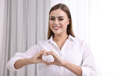 Happy woman showing heart gesture with hands indoors