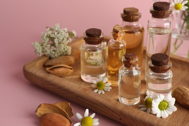 Aromatherapy. Different essential oils, flowers and almonds on pink background