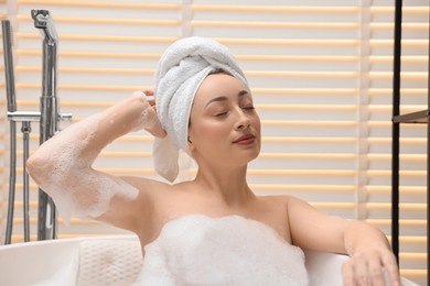 Photo of Beautiful woman taking bath with foam in tub indoors