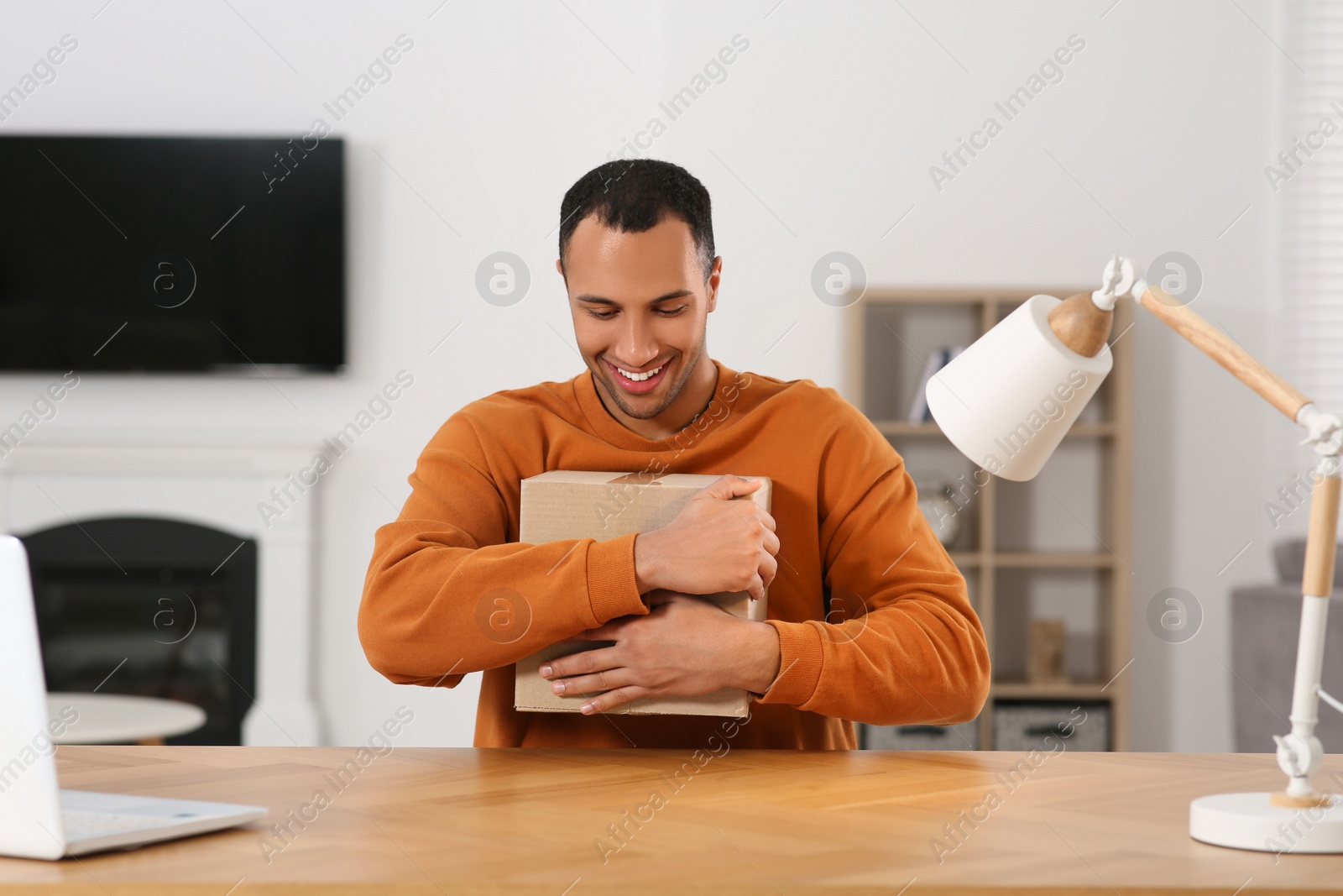 Photo of Happy young man with parcel at table indoors. Internet shopping