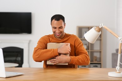 Happy young man with parcel at table indoors. Internet shopping