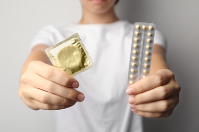 Photo of Young woman holding birth control pills and condom on light grey background, closeup. Safe sex concept
