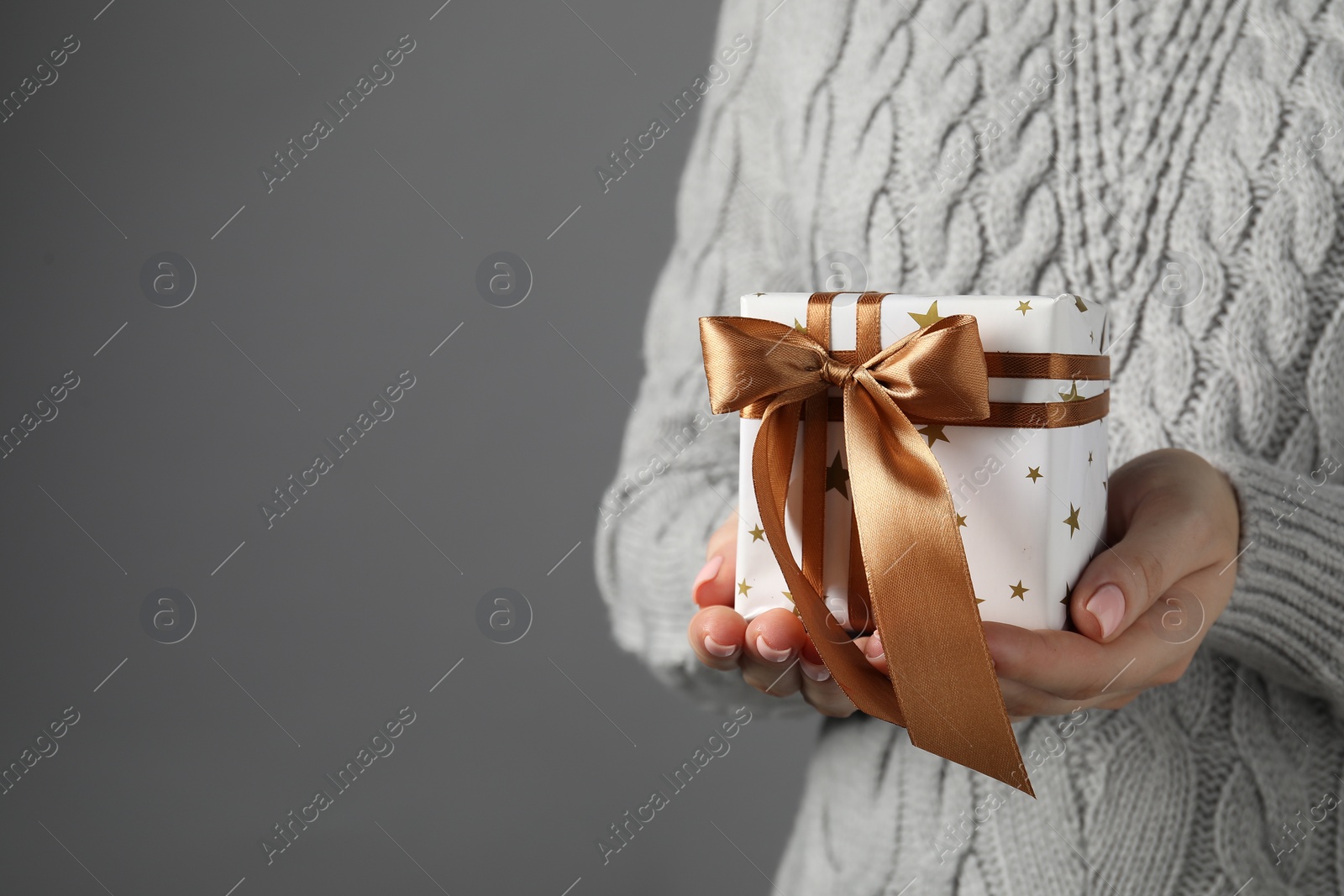 Photo of Christmas present. Woman holding gift box against grey background, closeup. Space for text