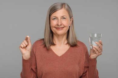 Senior woman with glass of water and pill on grey background