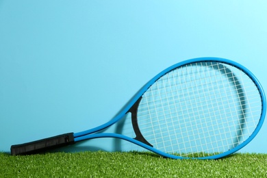 Tennis racket on on green grass against light blue background. Space for text