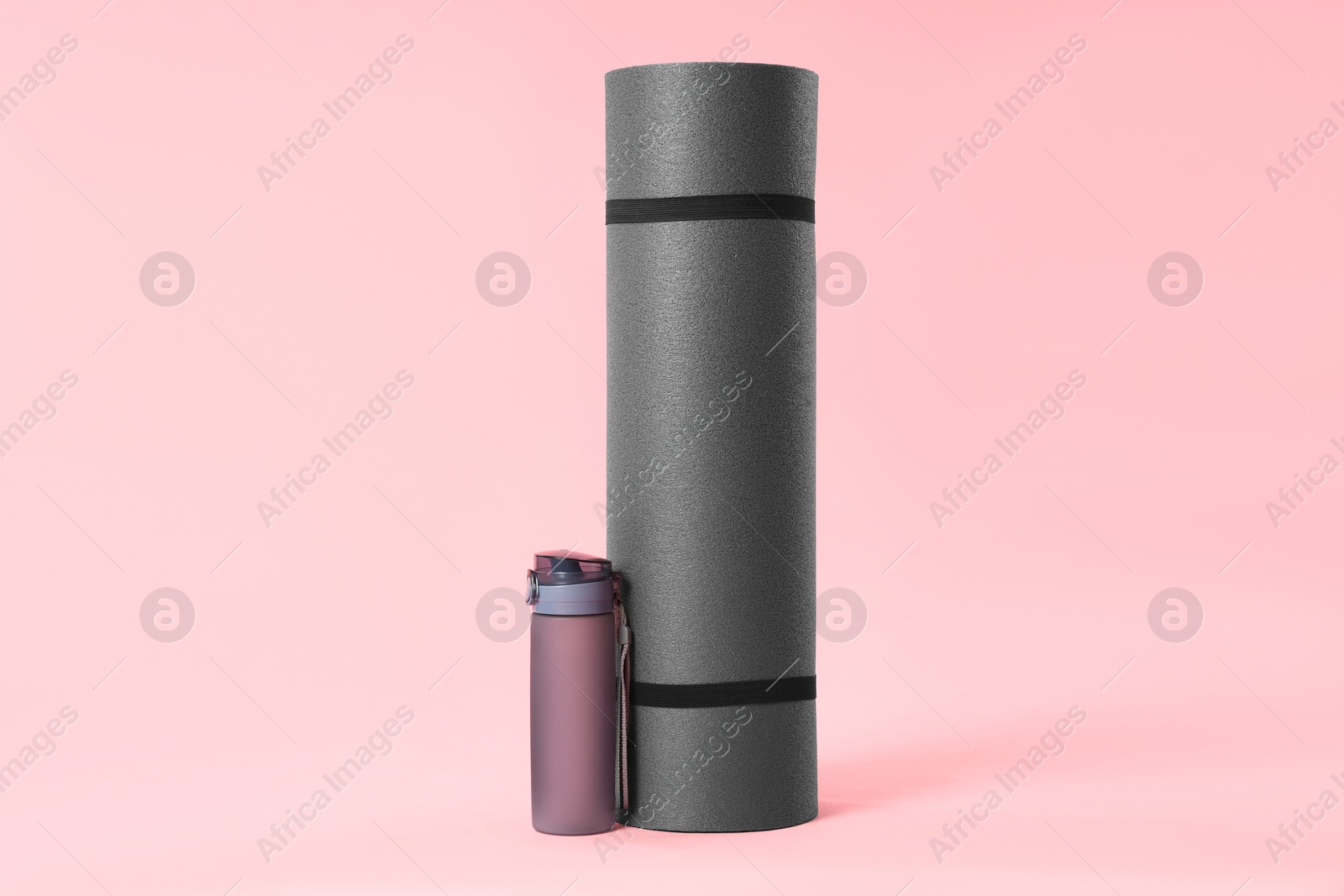 Photo of Grey yoga mat and bottle of water on pink background