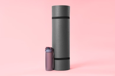 Grey yoga mat and bottle of water on pink background