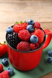 Photo of Many different fresh ripe berries in mug on wooden table, closeup