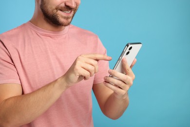 Man sending message via smartphone on light blue background, closeup