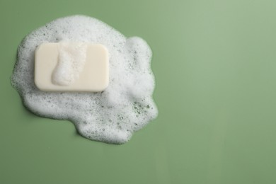 Photo of Soap and fluffy foam on green background, top view. Space for text