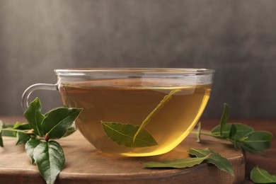 Photo of Cup of freshly brewed tea with bay leaves on wooden board, closeup