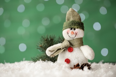 Photo of Snowman toy and Christmas decor on snow against blurred festive lights, closeup. Space for text