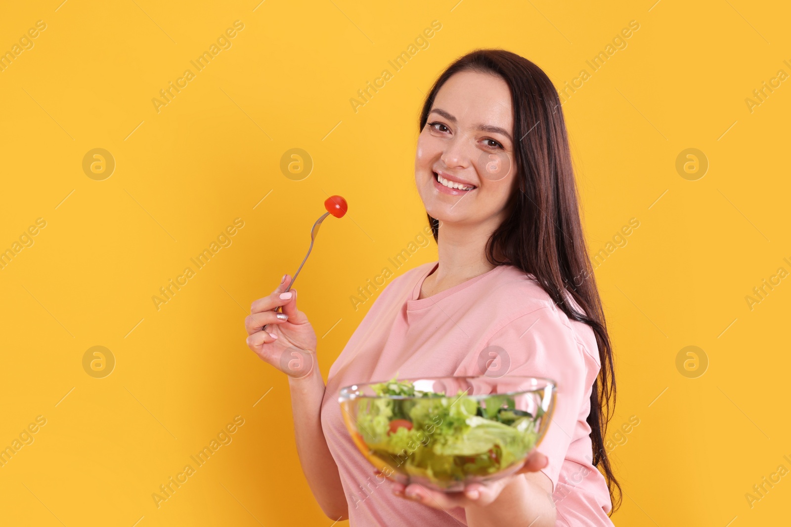 Photo of Beautiful overweight woman eating salad on yellow background, space for text. Healthy diet