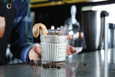 Barman holding White Russian cocktail at counter in pub, closeup