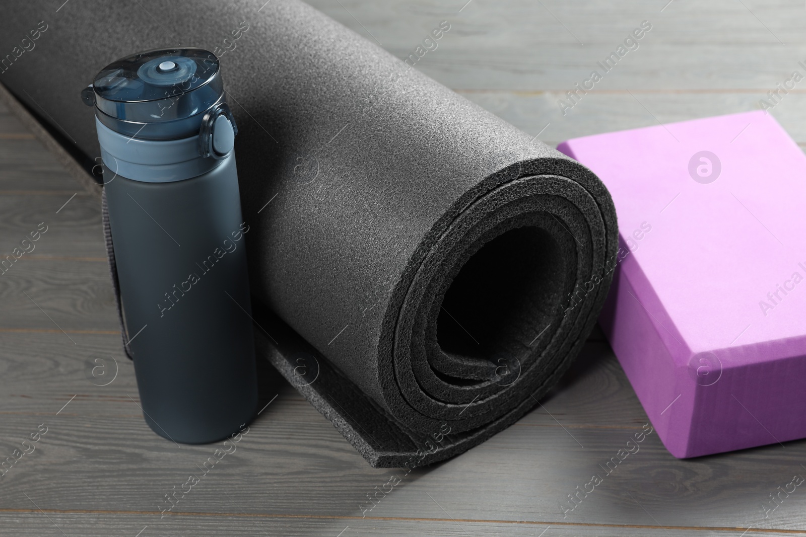 Photo of Exercise mat, yoga block and bottle of water on grey wooden floor