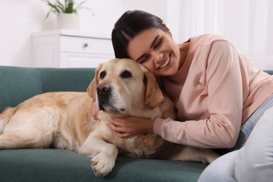 Happy woman with cute Labrador Retriever on sofa at home