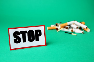 Card with word Stop near pile of cigarette stubs and burnt matches on green background. Stop smoking concept