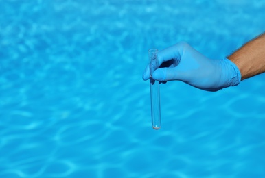 Man holding test tube with water against swimming pool on sunny day. Space for text