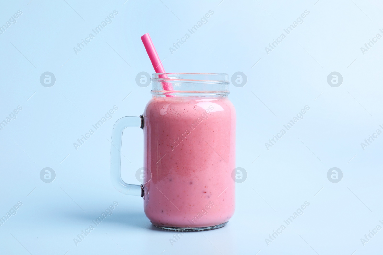 Photo of Mason jar with delicious berry smoothie on light blue background