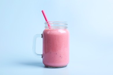 Mason jar with delicious berry smoothie on light blue background