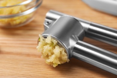Photo of One metal press with crushed garlic on wooden table, closeup