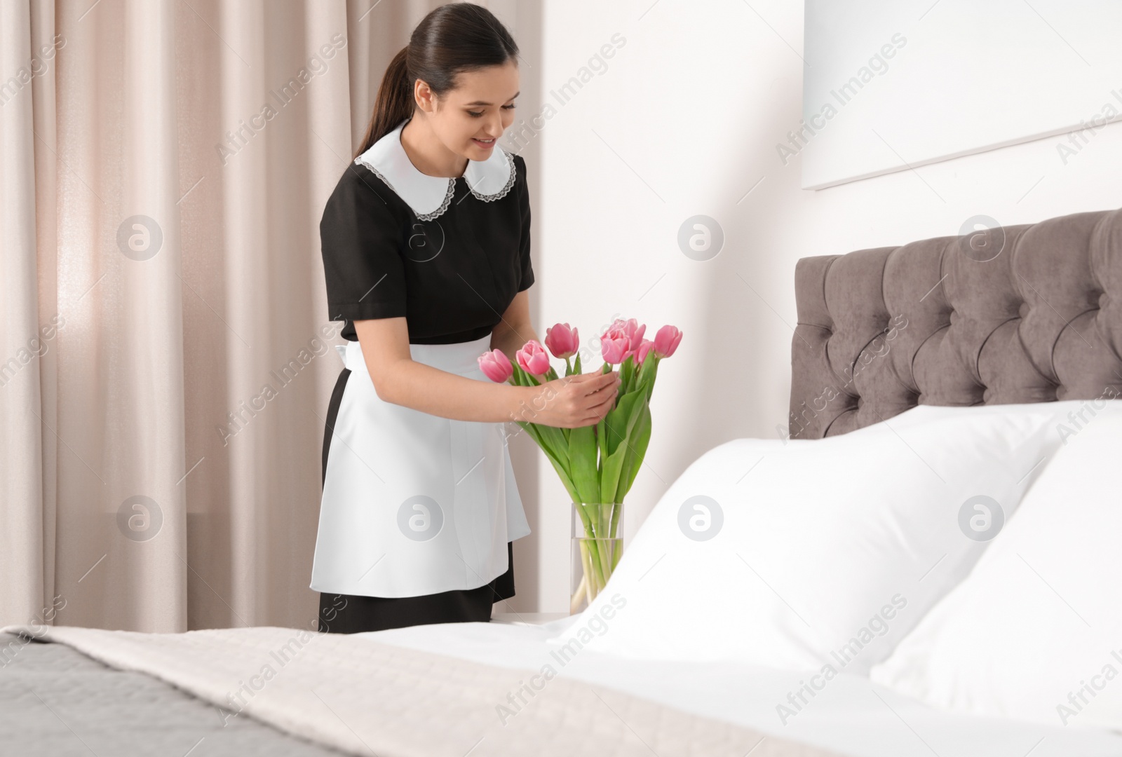 Photo of Young maid with flowers near bed in hotel room