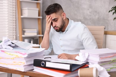 Overwhelmed man surrounded by documents at workplace in office