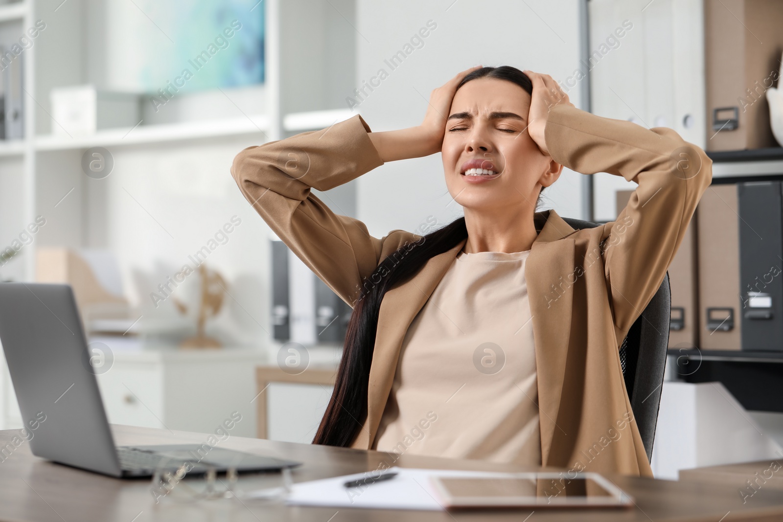 Photo of Woman suffering from headache at workplace in office