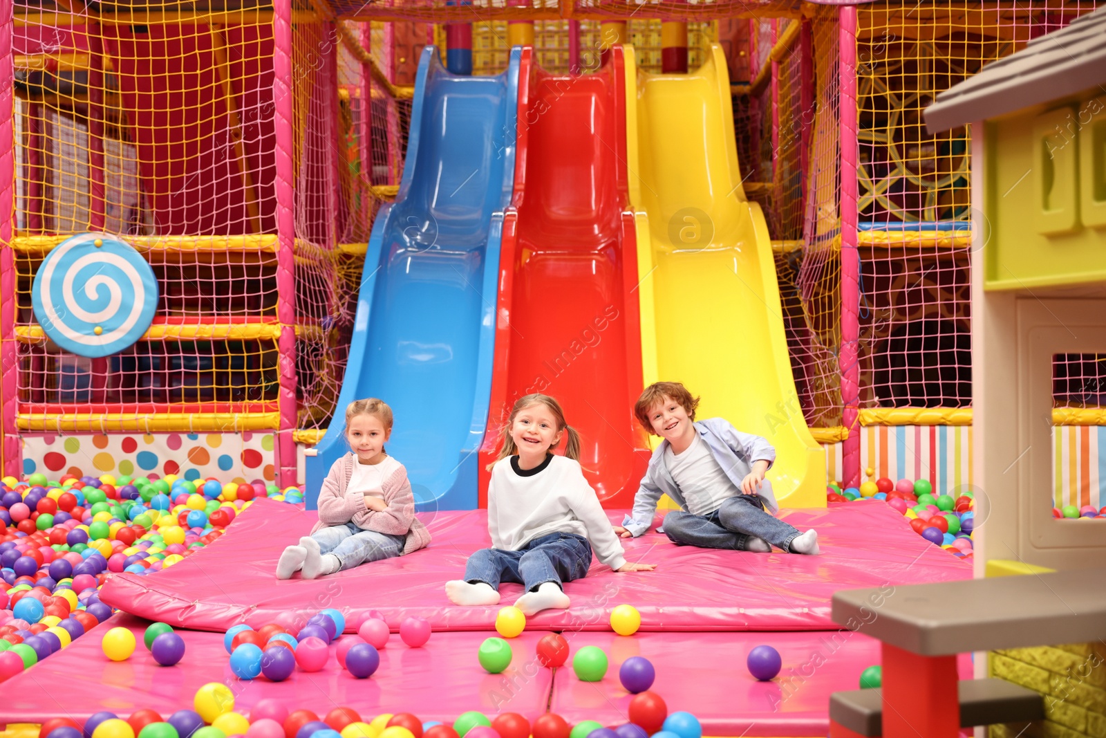 Photo of Happy kids playing in play room with slides, mats and ball pit