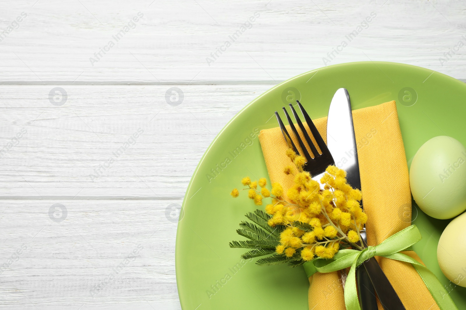 Photo of Festive Easter table setting with eggs and floral decor on white wooden background, top view. Space for text