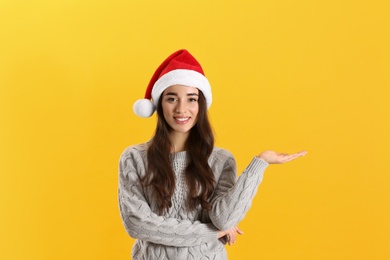 Beautiful woman wearing Santa Claus hat on yellow background