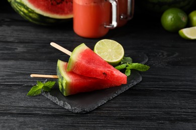 Photo of Slate board with cut juicy watermelon and lime on black wooden table